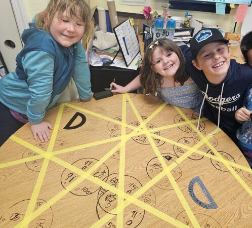 Children smiling at a table with angles they have measured using protractors